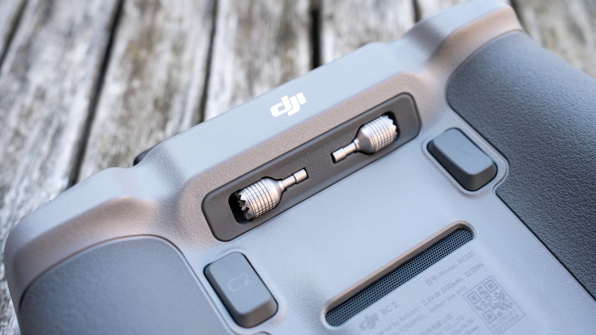 close-up of the underside of a drone controller with texutred dark grey grips, two trigger buttons and two accessories stowed near the top.