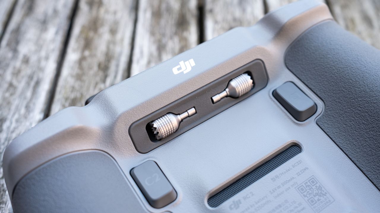 close-up of the underside of a drone controller with texutred dark grey grips, two trigger buttons and two accessories stowed near the top.