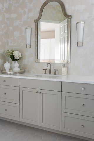 A beige bathroom with painted beige cabinets, a mirror and textured beige walls and