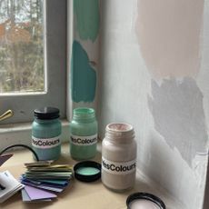 tester pots of green paints with splodges of them on the wall behind