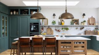 large kitchen with green cabines, wooden and white topped island, wall lights with small black shades and large brass pendant lights above island