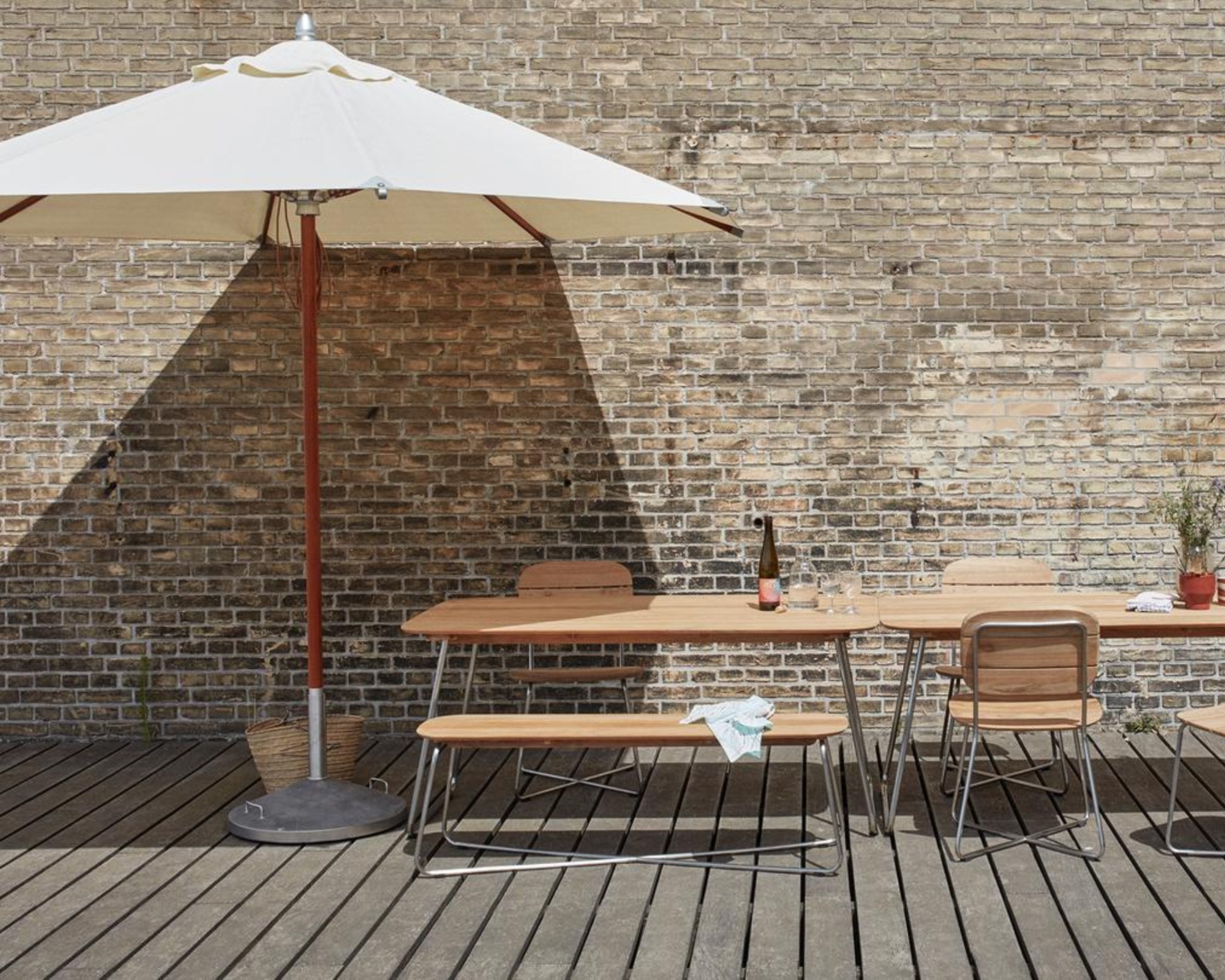 A cream and wood patio umbrella over an outdoor dining table and chairs