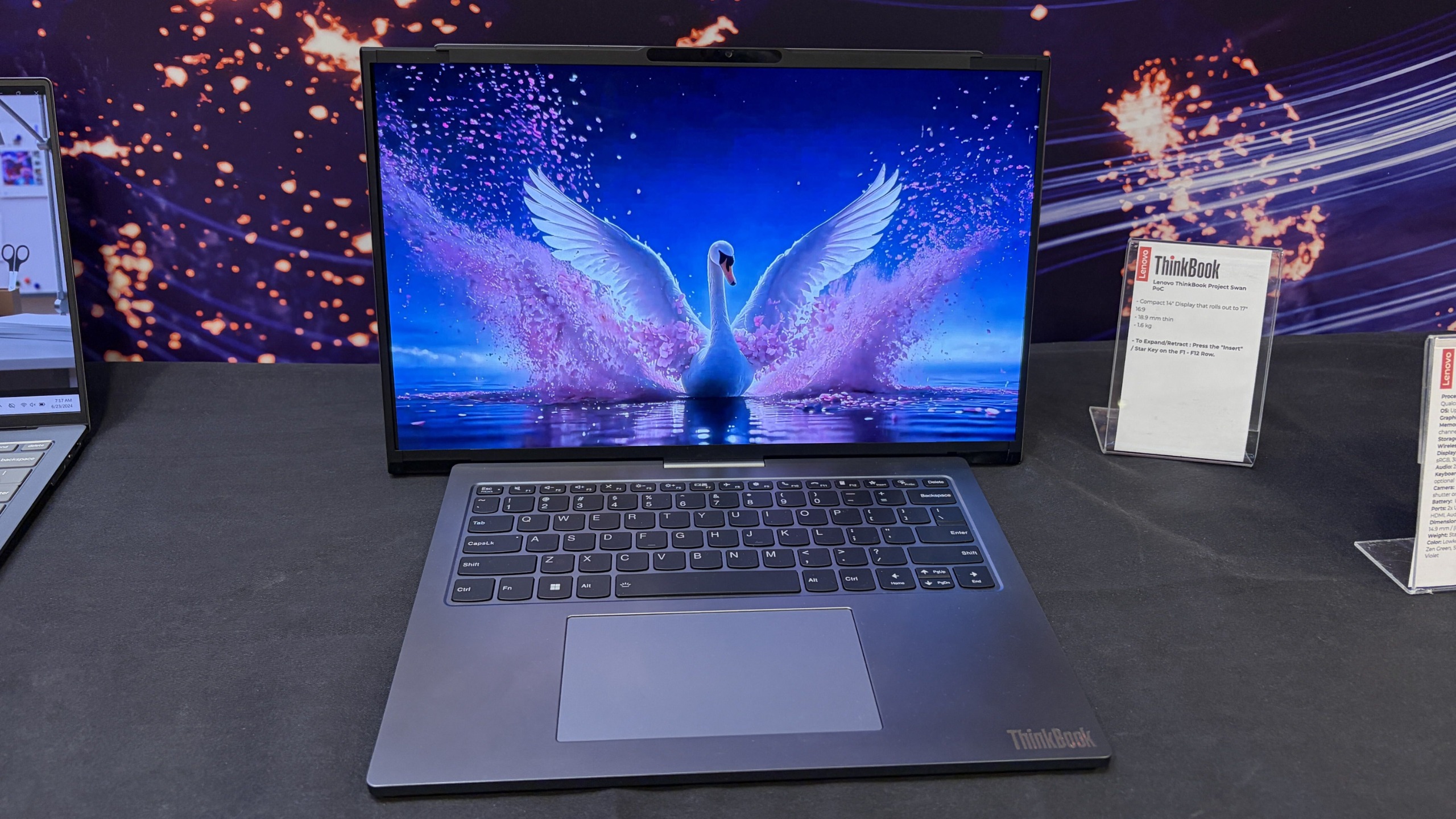 Lenovo Project Swan laptop on display, showing a vibrant swan with outstretched wings on a blue, starry lake scene at a tech exhibit.