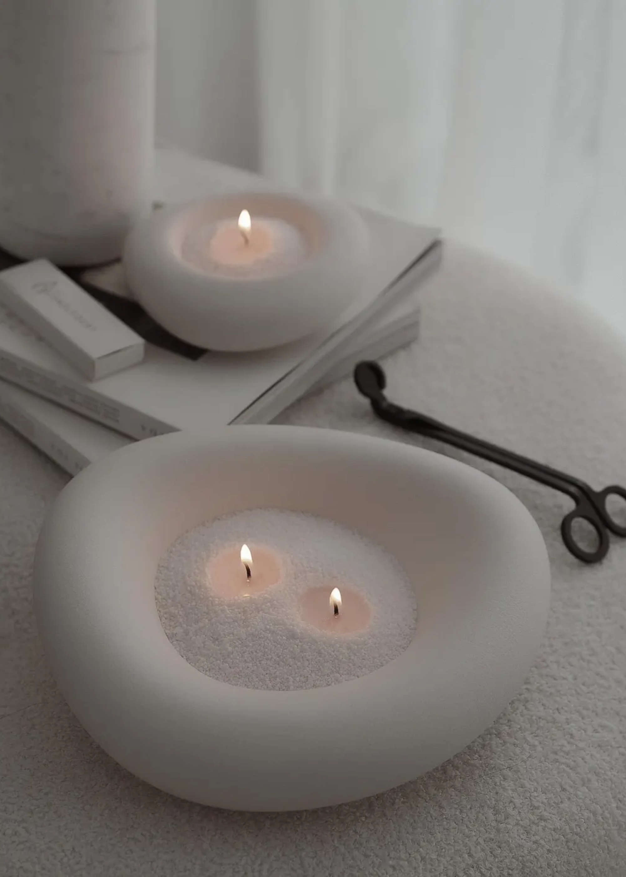 A pebble bowl for candle sand on a textured couch by a candle trimmer