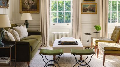 A bright, traditional living room featuring a forest green velvet sofa, olive green mid-century chairs, and twin green stools. Large sash windows are framed by cream drapes and a formal pelmet, with classical oil paintings on the walls.