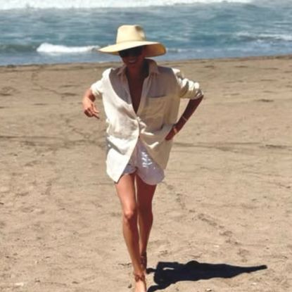 Meghan Markle on the beach wearing a linen shirt and shorts with her Cuyana hat