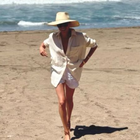 Meghan Markle on the beach wearing a linen shirt and shorts with her Cuyana hat