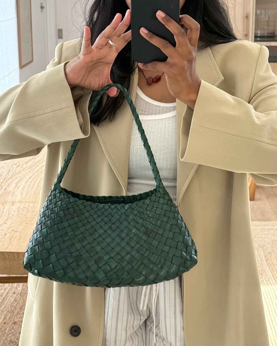Monikh Dale wearing a black pants, a black top, a camel coat and a woven leather bag.