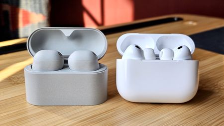 Sony WF-1000XM6 earbuds next to the Apple AirPods Pro 3, on a wooden table, in a versus-style format 