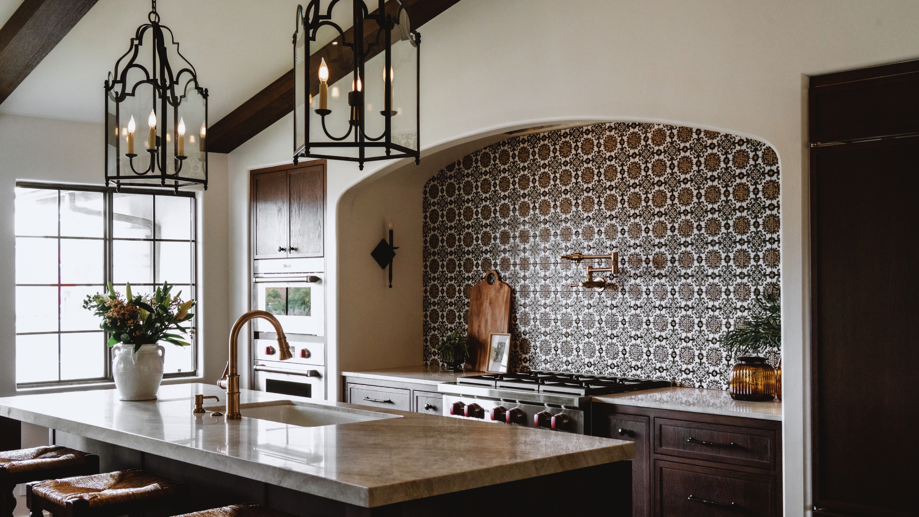A neutral kitchen with white walls, dark wood cabinets, patterned backsplash tiles, and statement lighting