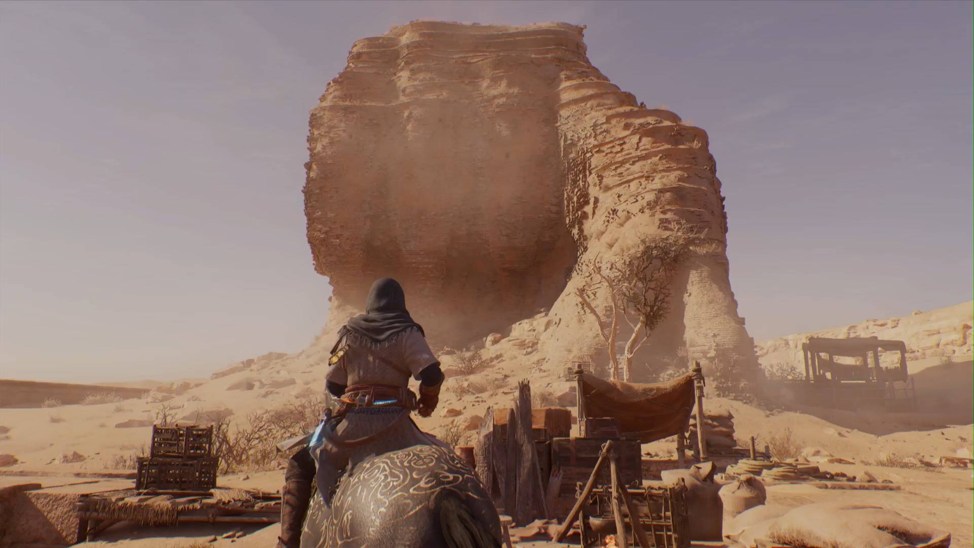 Assassin's Creed Mirage Basim jadący konno po pustyni i patrzący na wysokie ruiny skalne