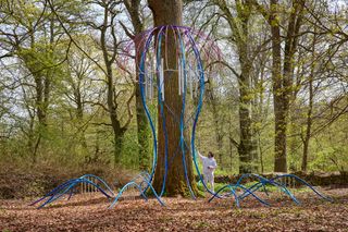 Man beside giant jelly fish sculpture around tree in forest