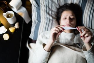 A sick person lying in bed with a thermometer.