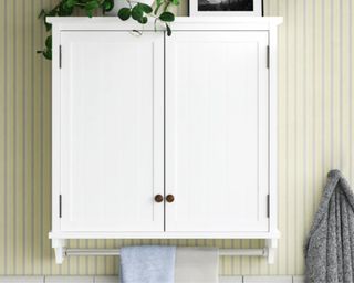 A white wall-mounted cabinet in a green bathroom with a towel rack beneath it