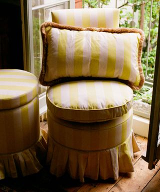 Yellow striped chair and pouffe both with a skirt in front of an open window