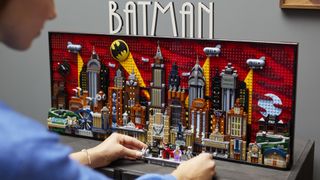 A woman places minifigures in front of the Lego Batman: The Animated Series set