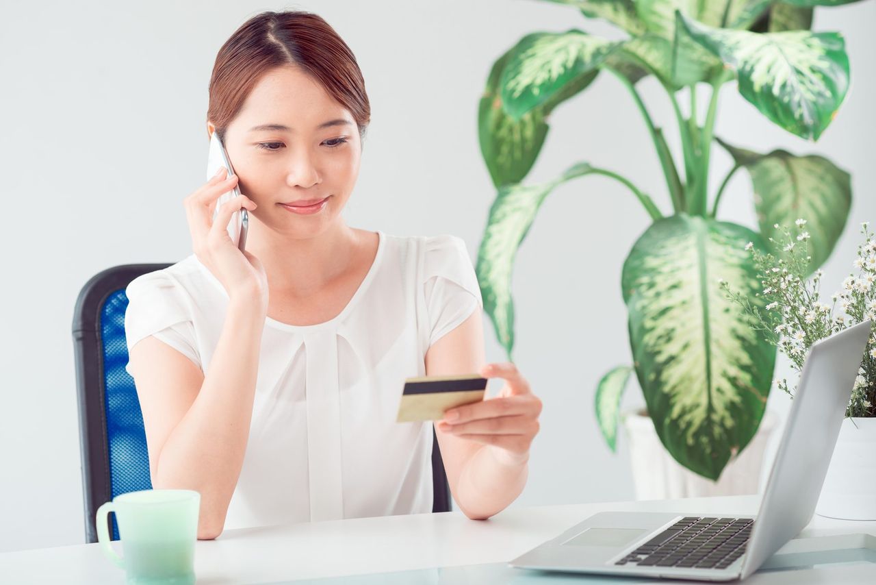 Lady On The Phone With Card In Hand Computer And Plant On Desk