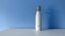 White water bottle with "W" logo in grey on the bottle and grey screw top, on white surface in front of a blue wall