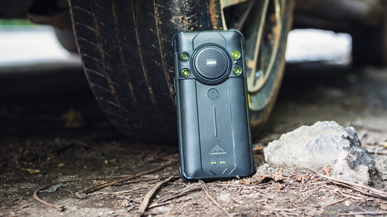 AGM H5 Pro leaning against a car tire on the ground outdoors