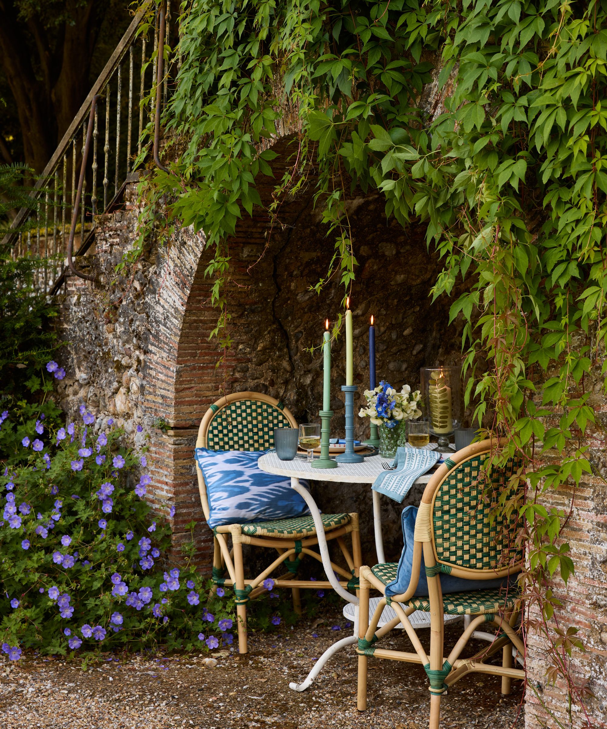 outdoor bistro set for two for a romantic dinner in a stone wall nook with foliage and green rattan bamboo furniture