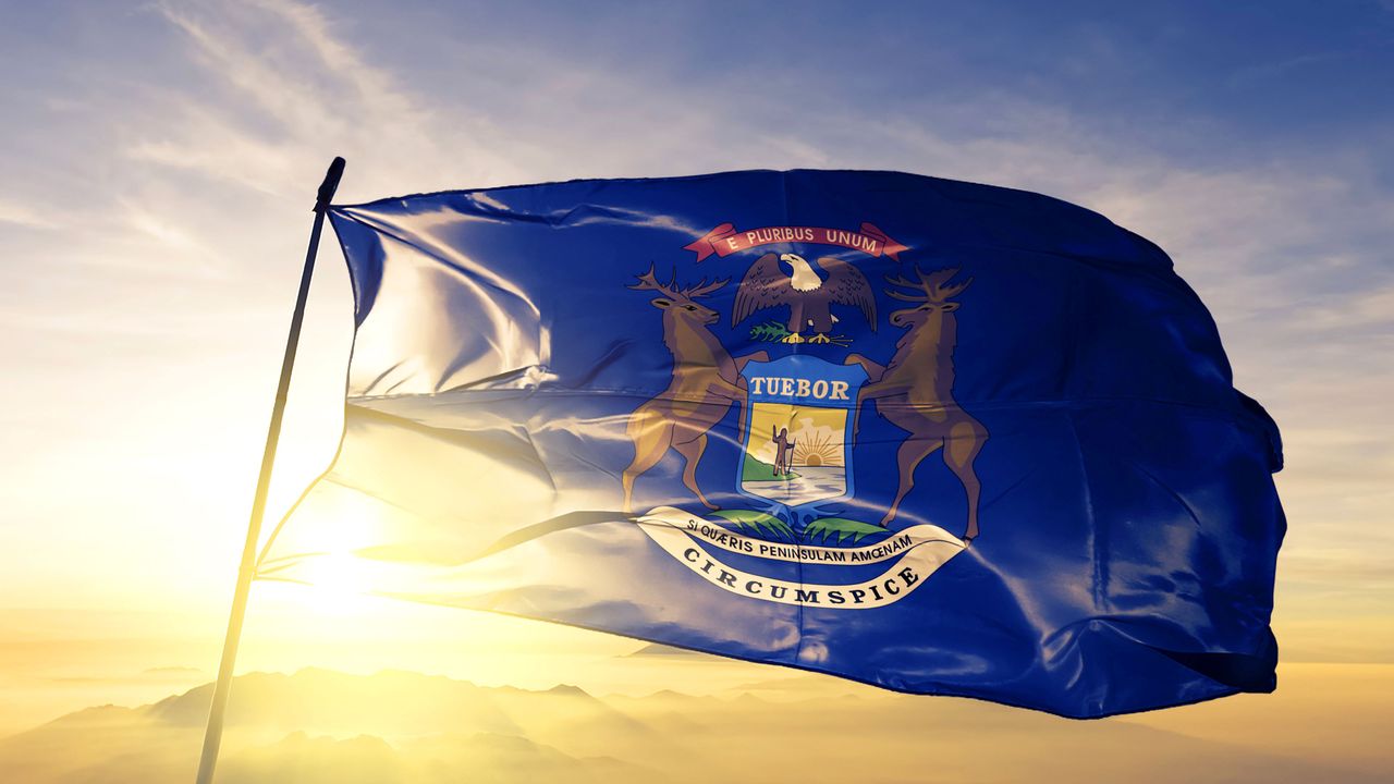 Photo of the Michigan state flag blowing in the wind in front of a sunrise for a Michigan state tax article.