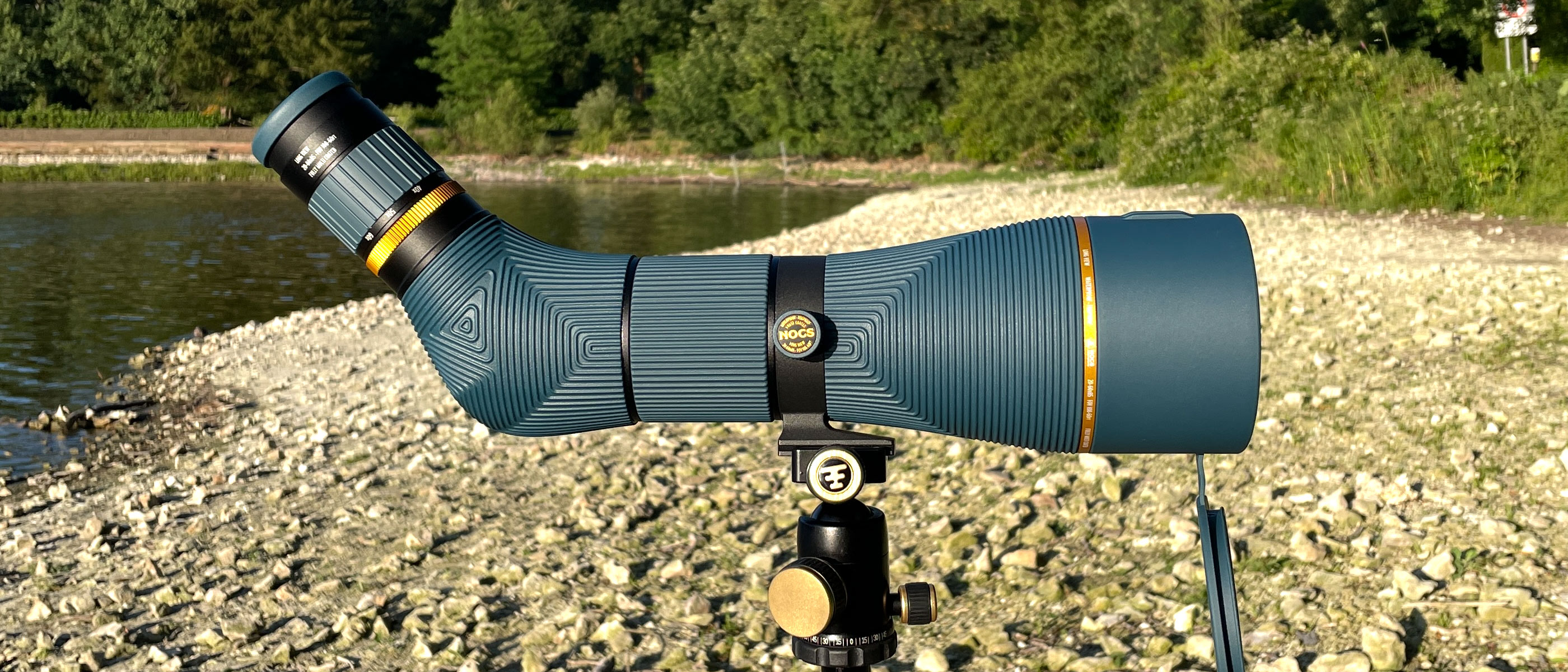 The Nocs Provisions Long View 85mm spotting scope mounted on a tripod, on a river bank.