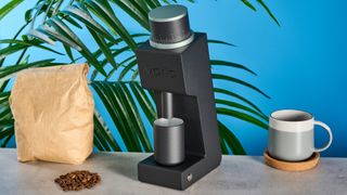 The Varia VS3 espresso grinder, next to a bag of beans and a coffee mug, on a stone work surface.