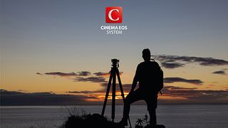 A man standing next to a tripod looking at a sunset