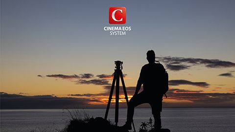 A man standing next to a tripod looking at a sunset