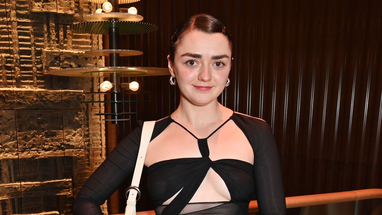 Maisie Williams stands in front of a plain backdrop