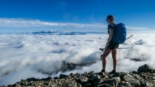 Jenny Tough standing at a mountain summit looking out over clouds