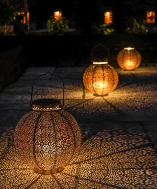 Solar powered Moroccan inspired lanterns casting patterned shadows along path.