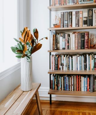 an organized wooden bookshelf in a white painted room with wooden flooring