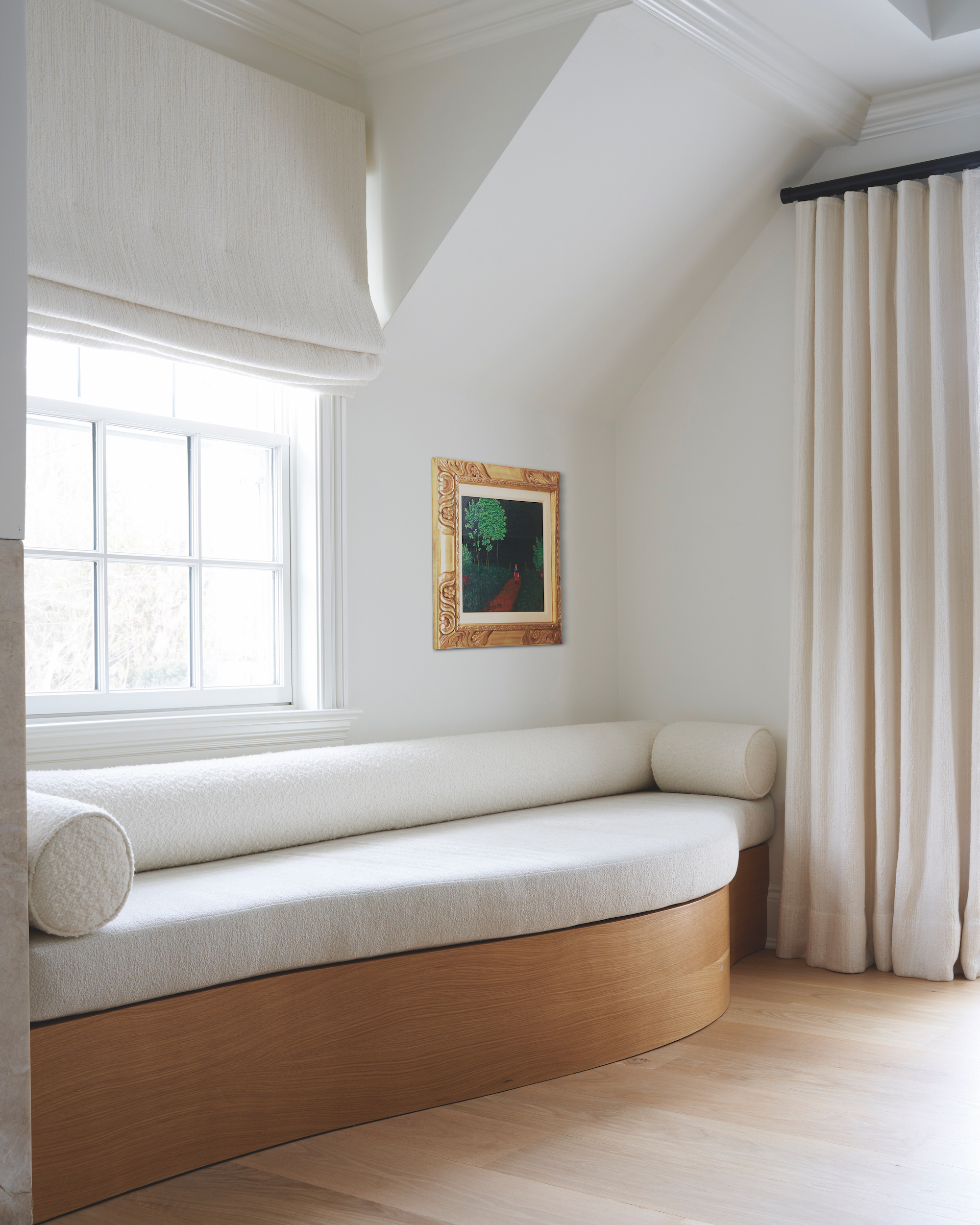 A cream colour drenched living space with wooden flooring that flows into the structure of the built in sofa, with cream upholstery and round cushions, with matching blinds and curtains around.