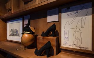 Hard wood shelves with 3 black rhino inspired heeled shoes on display with the sketch of the show on a white paper pinned to the shelf