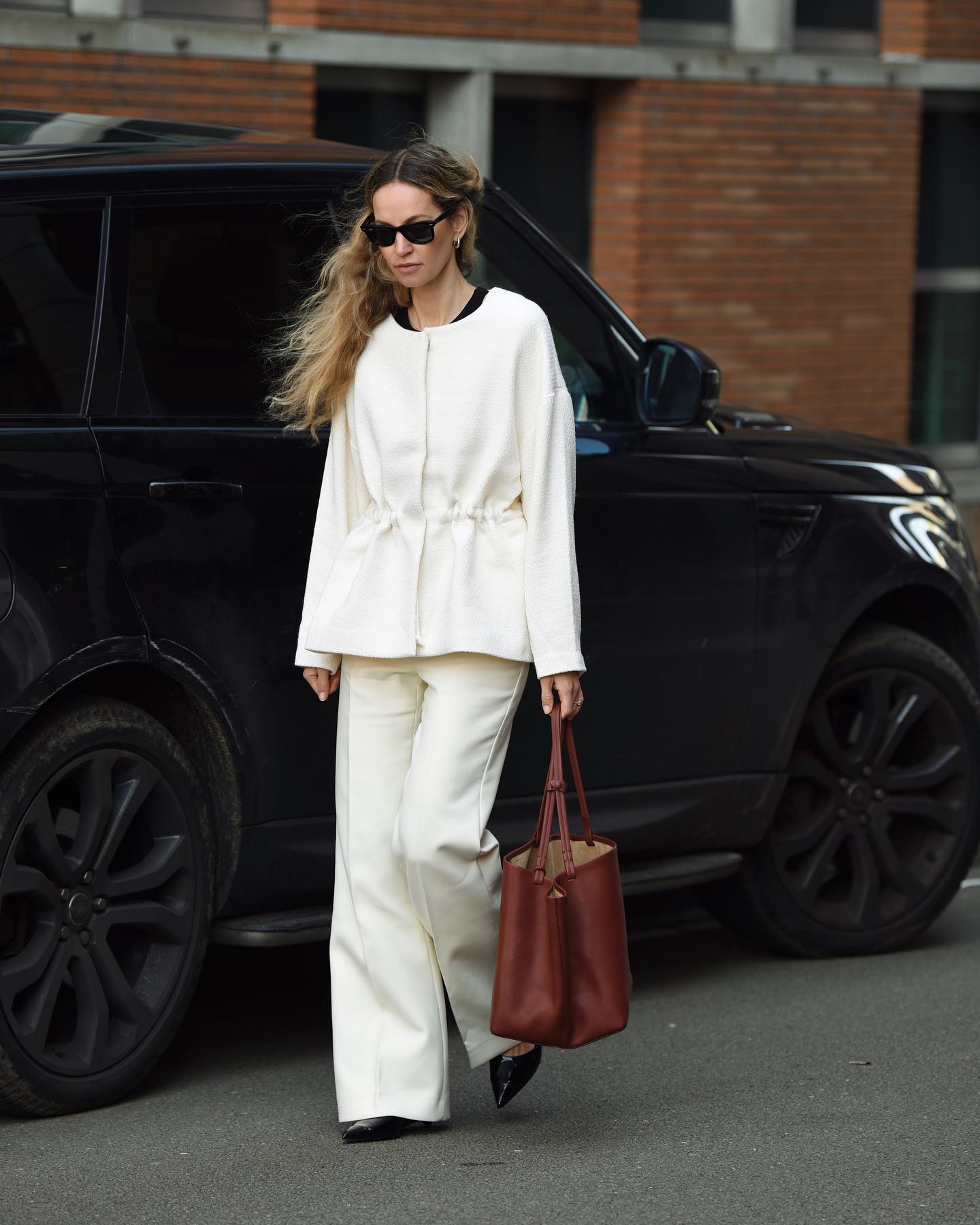 Influencer styles cream trousers with a cream blouse and a burgundy bag.