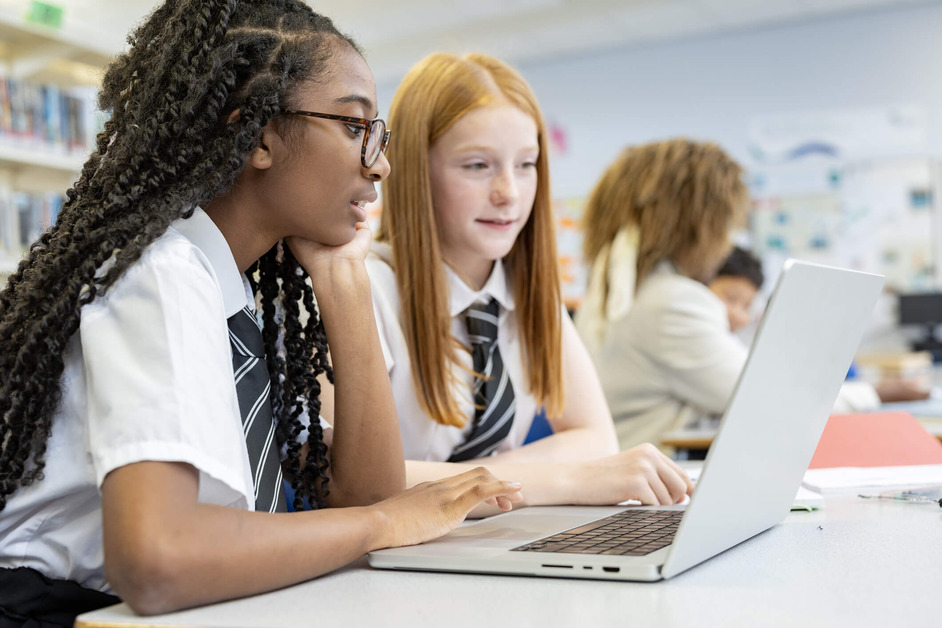 Two girls in school uniform are studying in front of a laptop. 