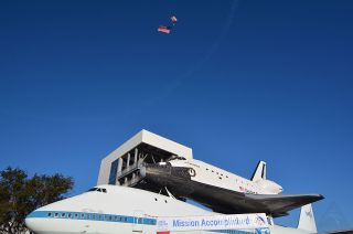 A Re/Max skydiver, trailing an American flag, soars over the space shuttle Independence at Space Center Houston on Jan. 23, 2016.