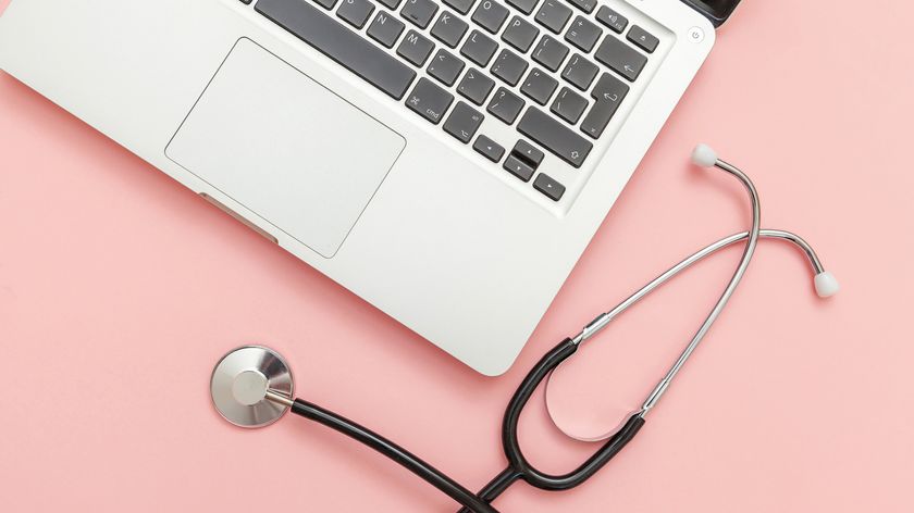 A stethoscope next to a laptop on a pink background