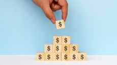 Wooden blocks with dollar signs on them are stacked in the shape of a pyramid.