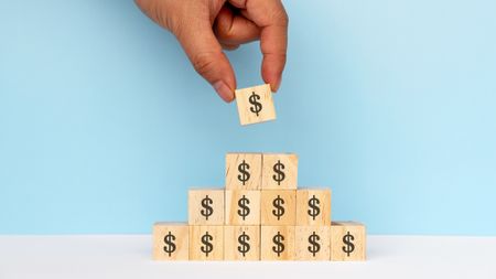 Wooden blocks with dollar signs on them are stacked in the shape of a pyramid.