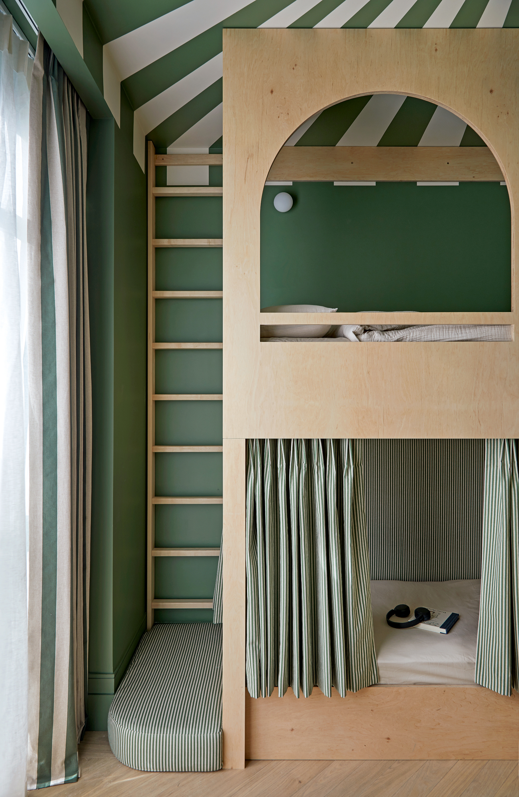 Children's room with green walls and green and white striped ceiling, plywood bunk beds with green and white striped curtains, and a ladder