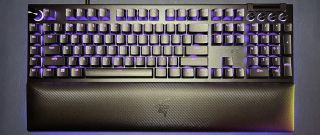 full-size black Razer keyboard with purple lighting and wrist rest against navy blue background