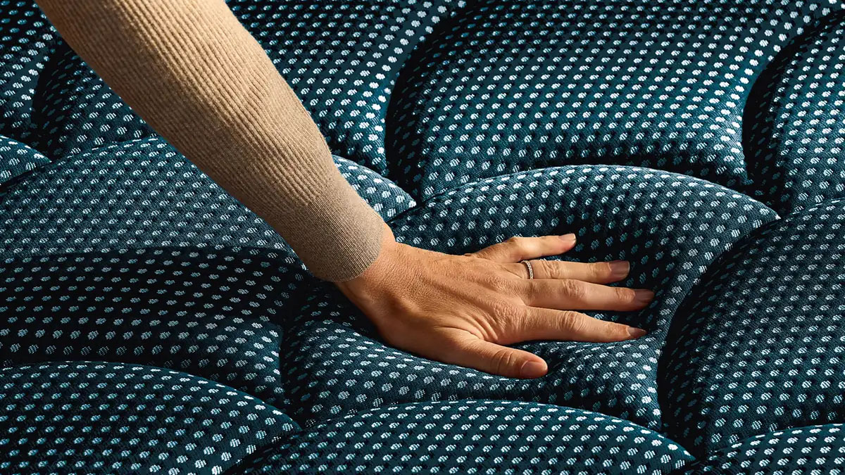 A close up of a hand pressing into the surface of a DreamCloud PressureSmart Mattress