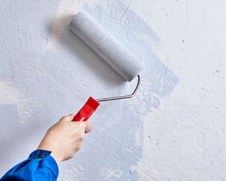 Home painter is painting walls with paint roller and paints during renovation