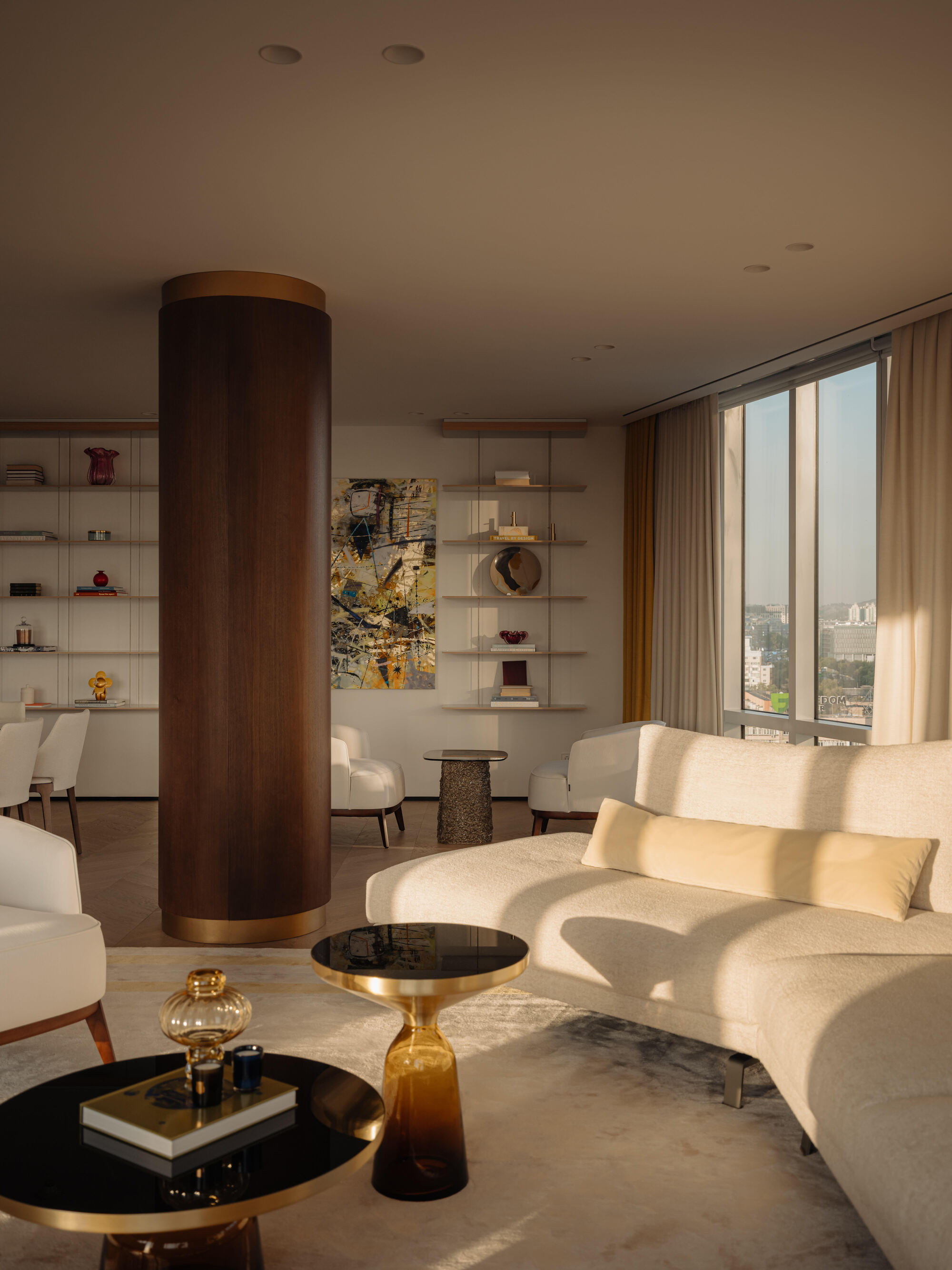 beige living room with timber column, display shelves, a cream sofa, cream patterned rug, two round coffee tables, and cream curtains