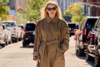 Courtney wears a long beige trench coat and black sunglasses.