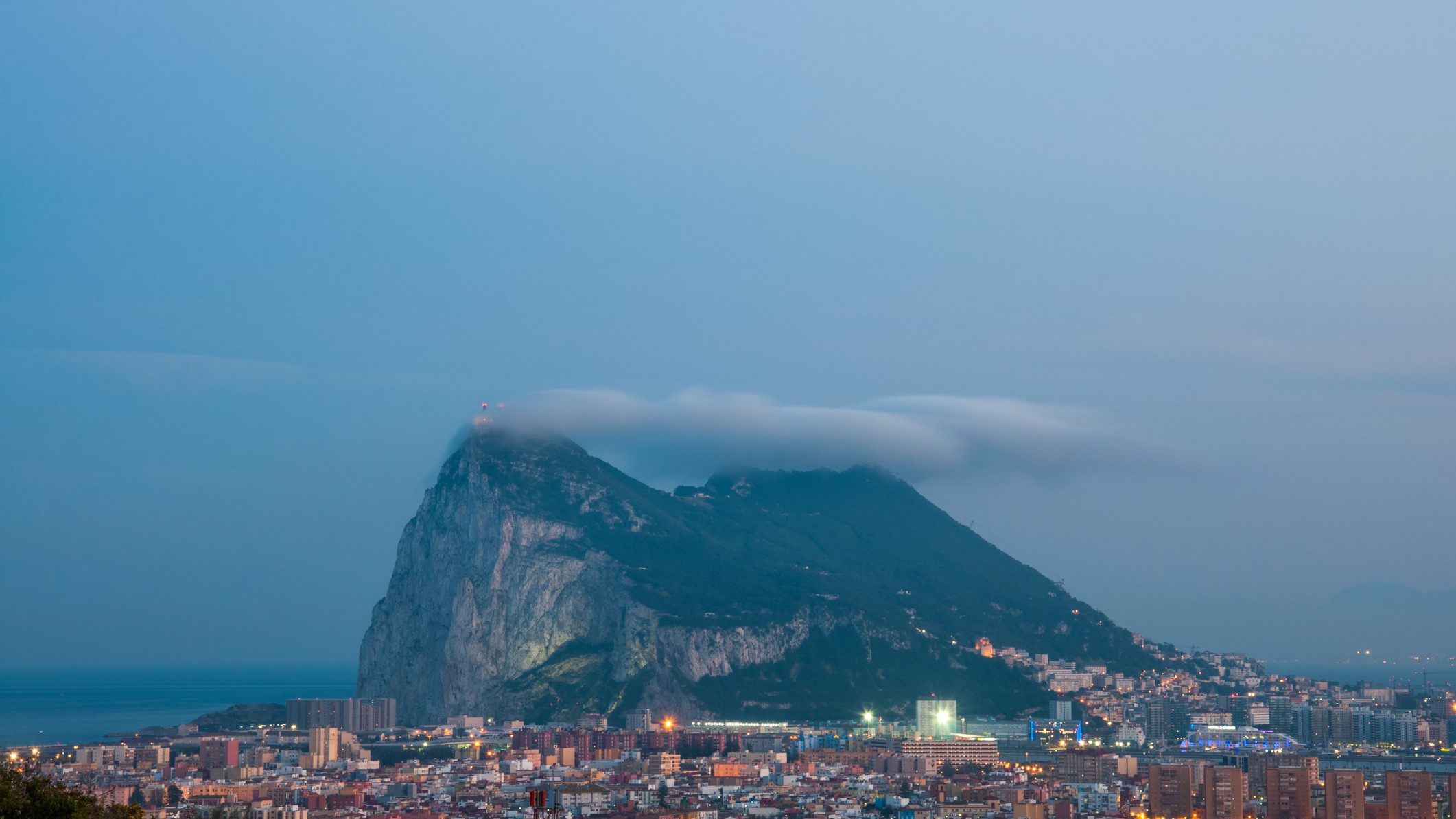 The Rock of Gibraltar at Dusk with the Levante Cloud forming above it. In the foreground is the sprawling border town of La Linea de la Concepción, Cadiz, Spain.