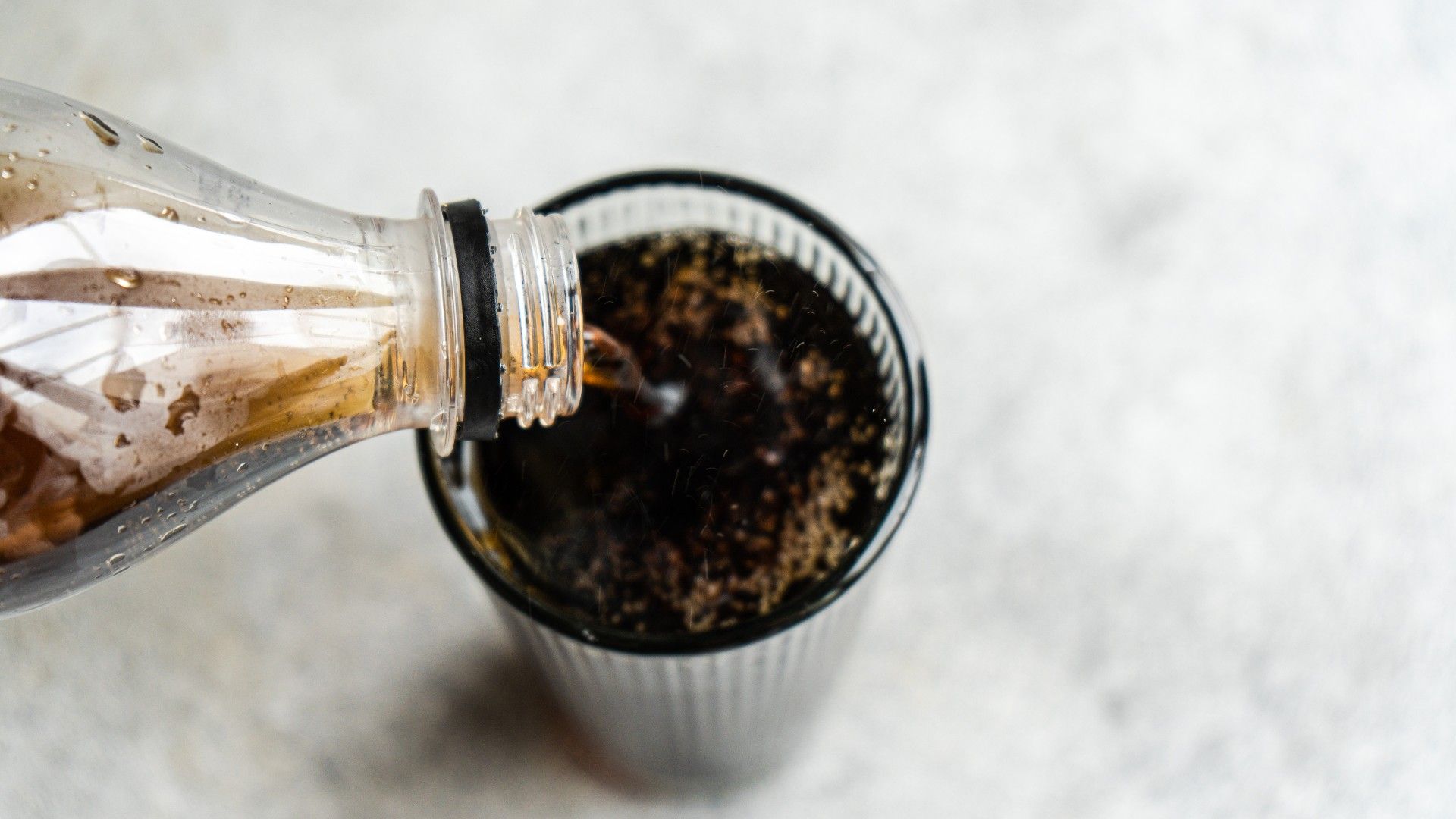 person pouring a glass of Coca Cola into a glass on a kitchen worksurface