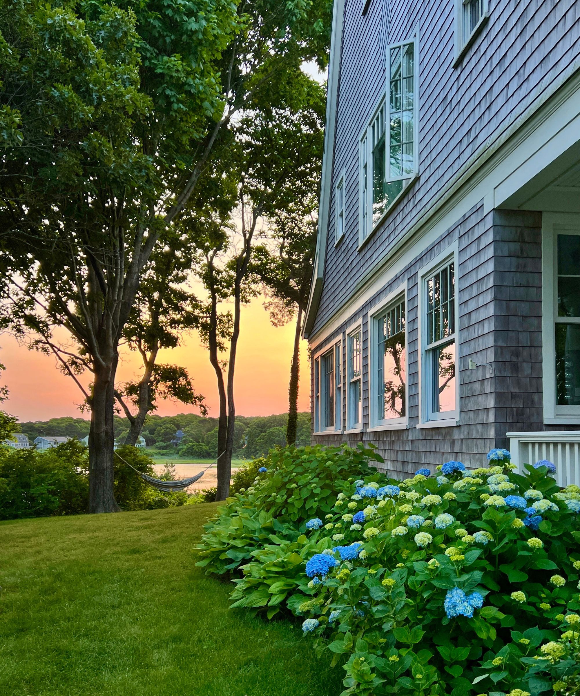 Shingle style home with lawn overlooking lake with hammock